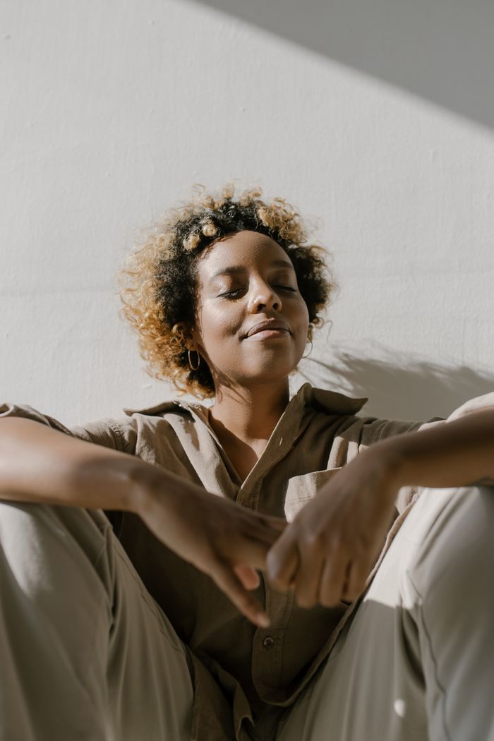 A serene woman with closed eyes enjoying the sunlight indoors, expressing contentment and relaxation.