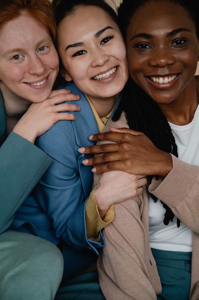 Three diverse women smiling and embracing, symbolizing friendship and unity.